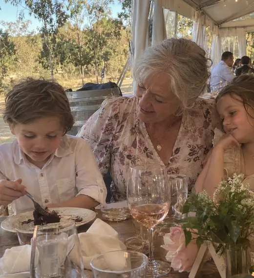 A grandmother at a reception table with two children, one of them eating cake